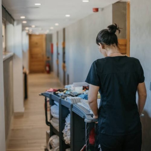 Young hotel maid in uniform pushing chambermaid trolley down the hotel corridor