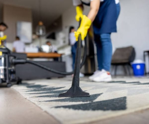 Close-up on a professional cleaner vacuuming a carpet while working at an apartment - housework concepts